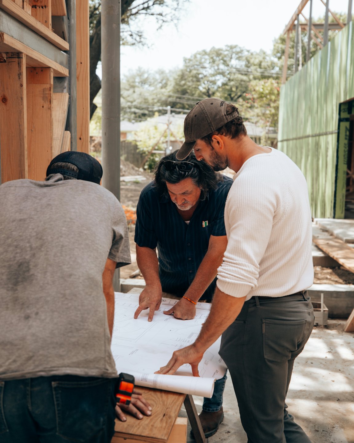 Three construction professionals review blueprints at an outdoor site.